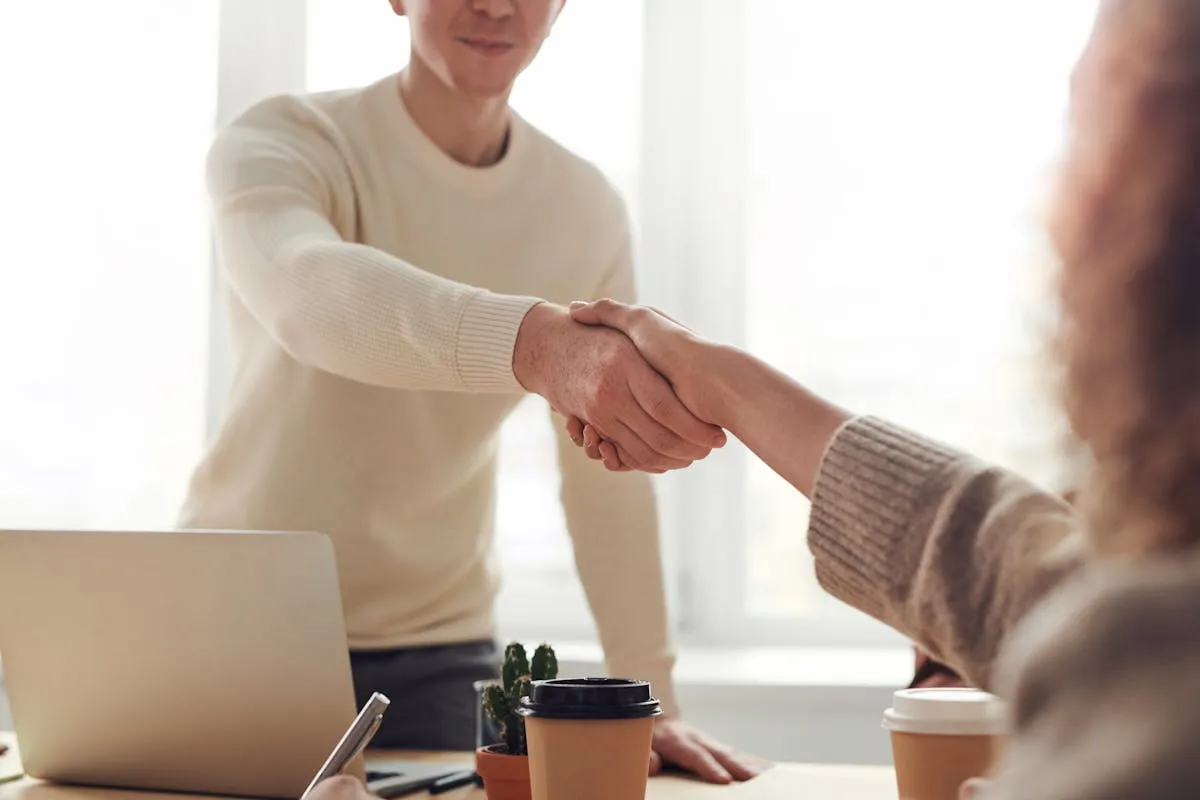 Zwei Personen reichen sich an einem Tisch die Hand